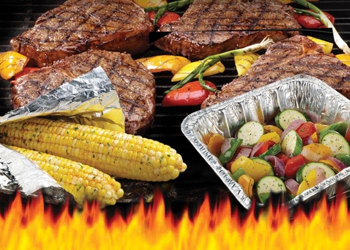 Foil pan with vegetables on the grill surrounded by more vegetables